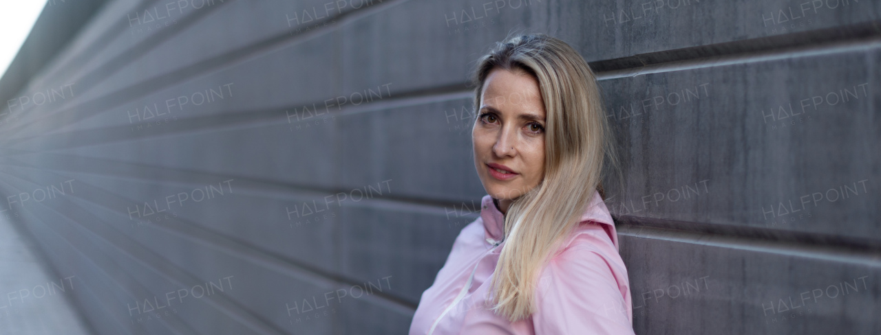 Young blond woman standing in front of a concretewall. Wide photography.