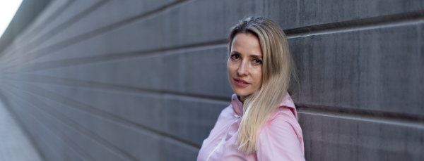 Young blond woman standing in front of a concretewall. Wide photography.