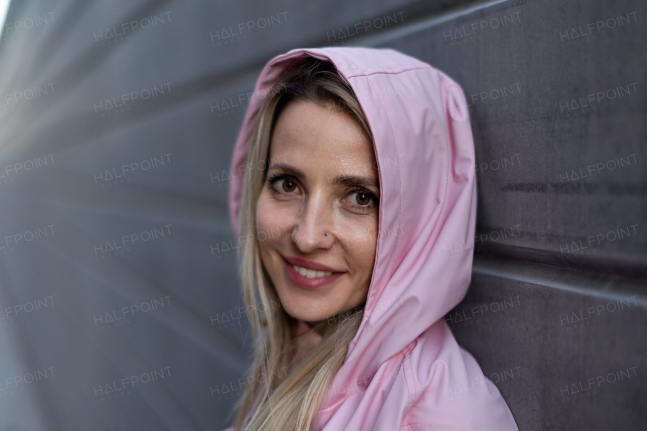 Young blond woman with hood on head, standing in front of a brick wall.