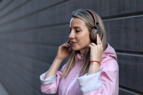 A young woman in city with headphones listening music. Side view.