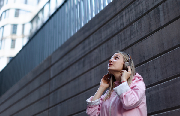 A young woman in city with headphones listening music. Side view.