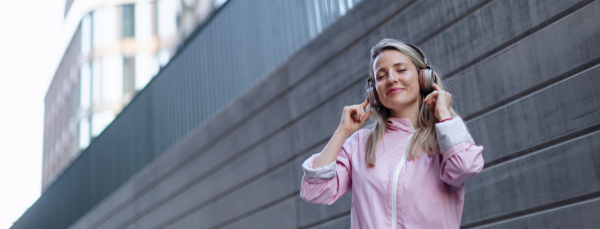 A young woman in city with headphones listening music. Low angle view.