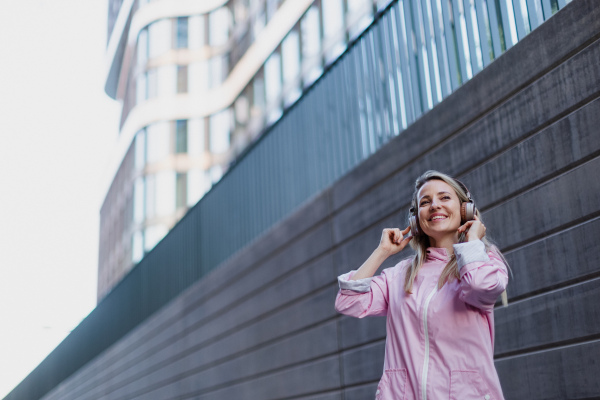 A young woman in city with headphones listening music. Low angle view.