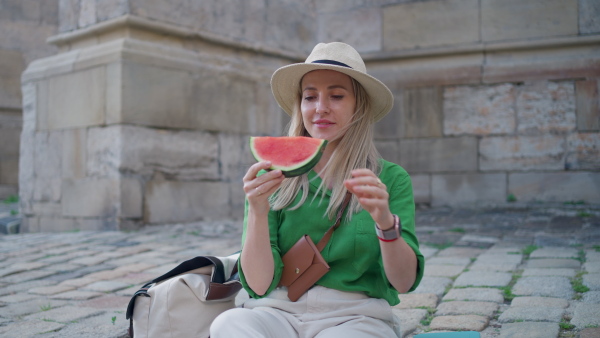 A young woman traveller eating watermelon in street during hot sunny day, summer vacation trip concept.