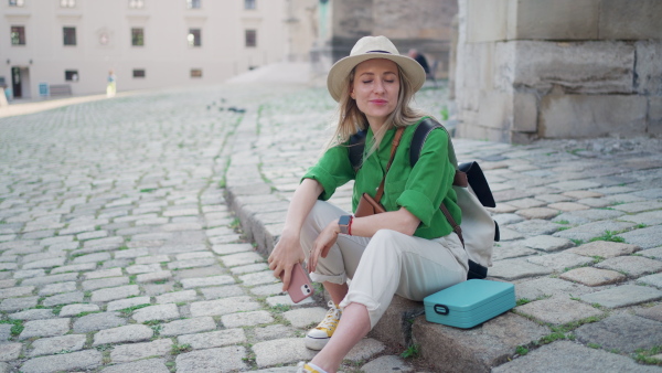 Young blond woman travel alone in old city centre, sitting and using smartphone.