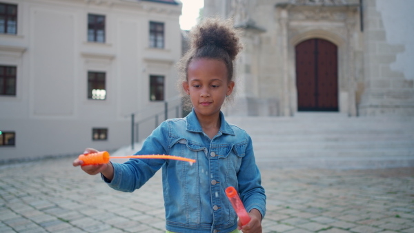 A little multiracial girl playing outdoor with bubble blower.