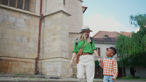 A mid adult mother holding his little multiracial son and walking in town in summer together.