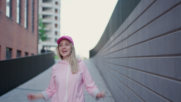 A young happy woman in fashion clothes walking in city concrete wall.