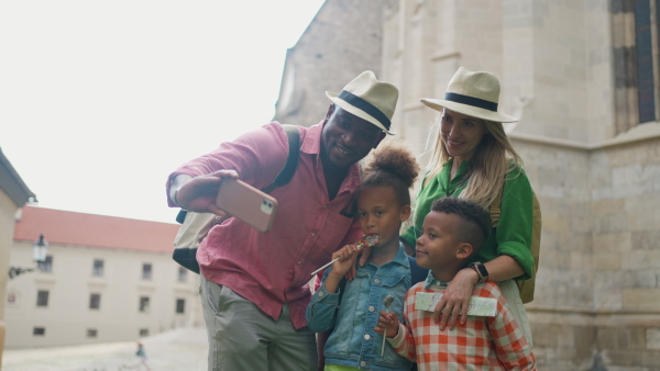 A multiracial family travelling together with small kids. Taking selfie in old city cetre.