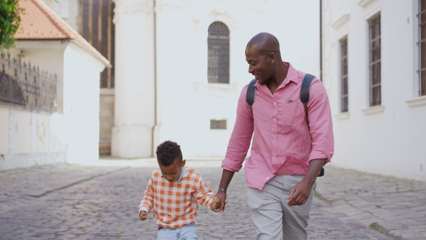 A multiracial father holding his little son and walking in town in summer together.