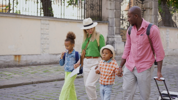 Happy multiracial family travel together with suitcases, walking in old city centre.