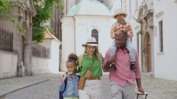 Happy multiracial family travel together with suitcases, walking in old city centre.