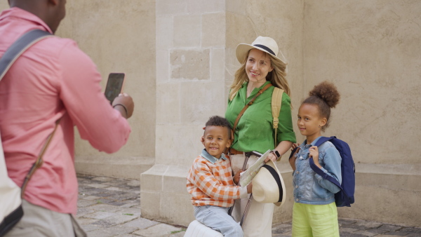 A multiracial family travelling together with small kids. Father taking photo of wife and kis in old city cetre.