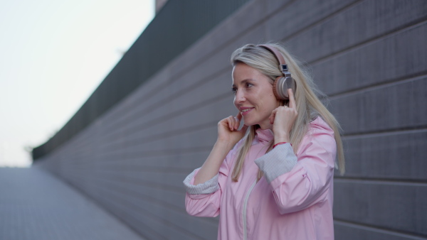 A young woman in city with headphones listening music. Low angle view.