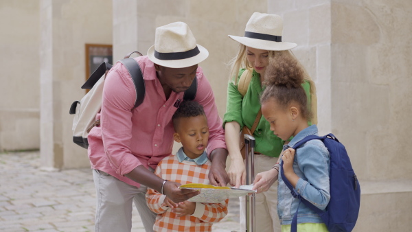 Multiracial family travel together in old city centre, looking at a map.