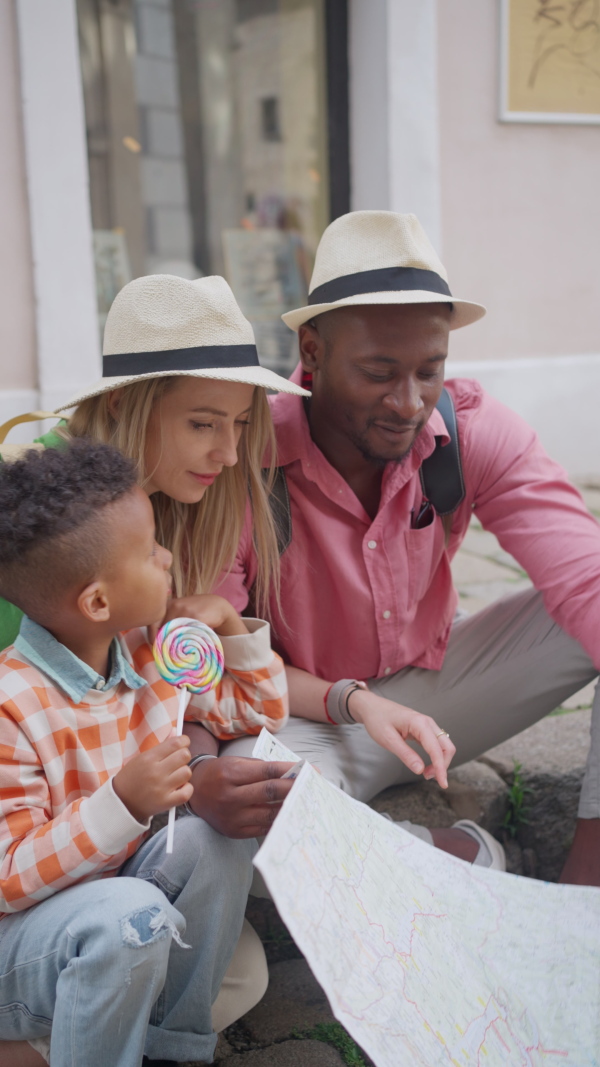 Multiracial family travel together in old city centre, looking at a map.