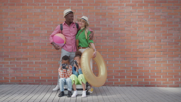 Multiracial family travelling together with small kids. Posing in front of a brick wall.