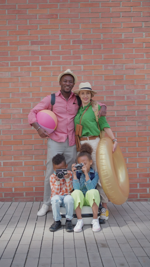 Multiracial family travelling together with small kids. Posing in front of a brick wall.