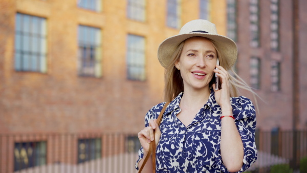 A mid adult woman walking in summer in town and calling on mobile phone.