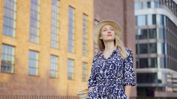 A young woman in dress and hat walking in summer in town.