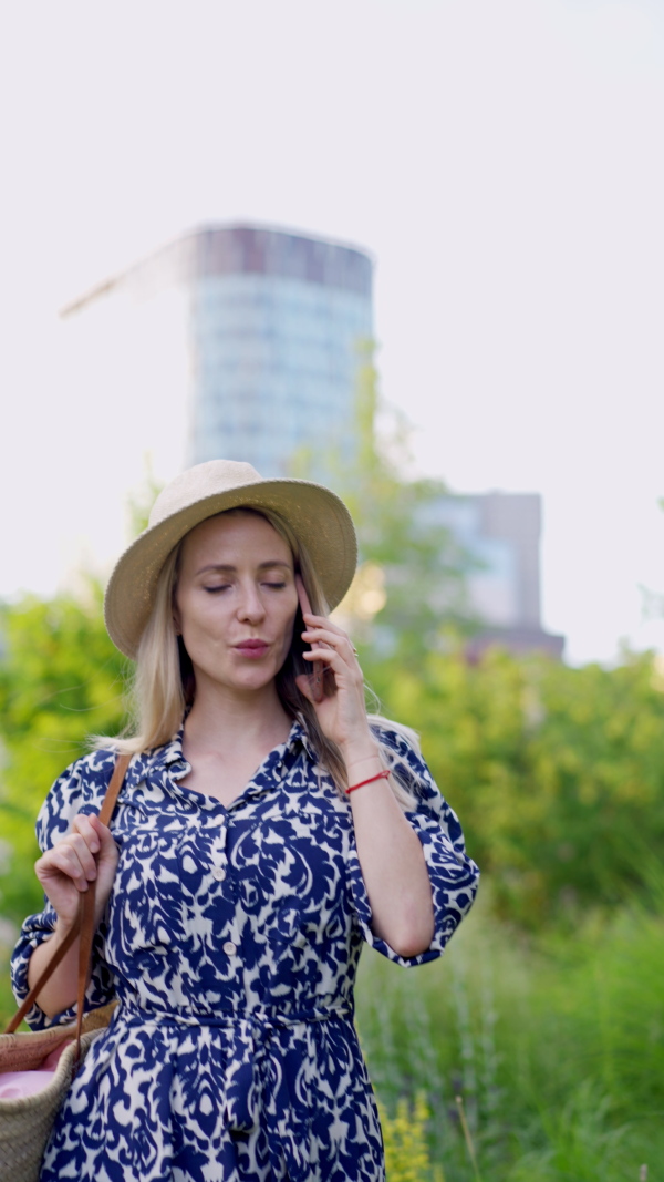 A mid adult woman walking in summer in town and caaling on mobile phone.