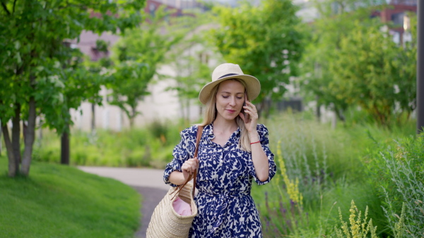 A mid adult woman walking in summer in town and calling on mobile phone.