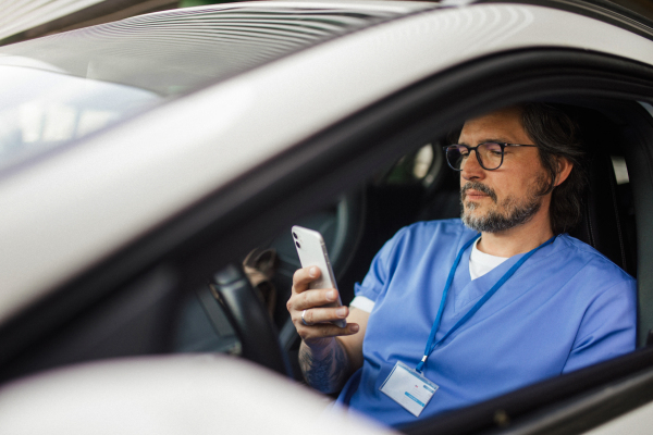 Doctor getting into car, going home from work after long shift, texting. Work-life balance of healthcare worker.