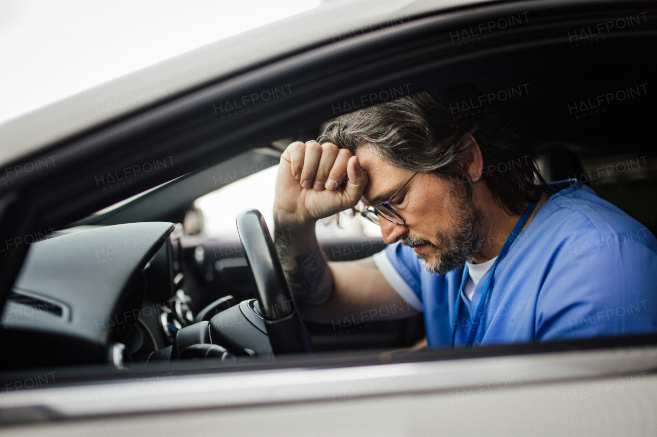 Doctor in car, feeling exhausted and sad. Overwhelmed caregiveer after hard work day in clinic, hospital. Work-life balance of healthcare worker.