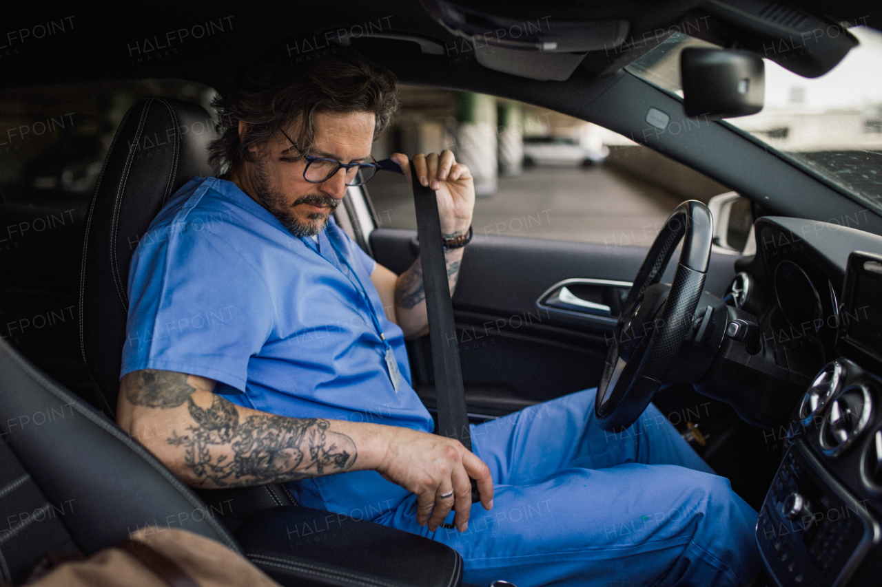 Handsome doctor getting into car, fastening a car seat belt. Work-life balance of healthcare worker.