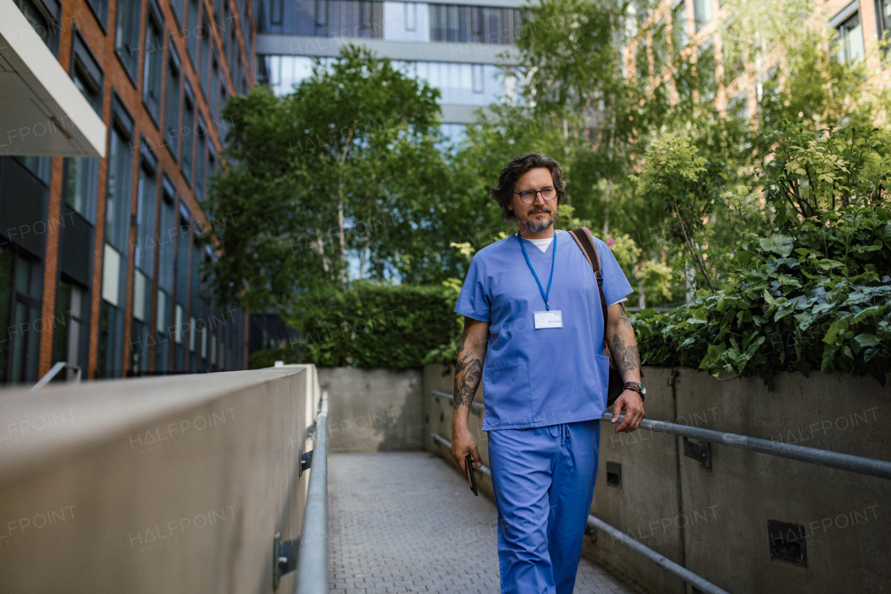 Male n uniform going home from work, walking in front of hospital building. Work-life balance of healthcare worker.