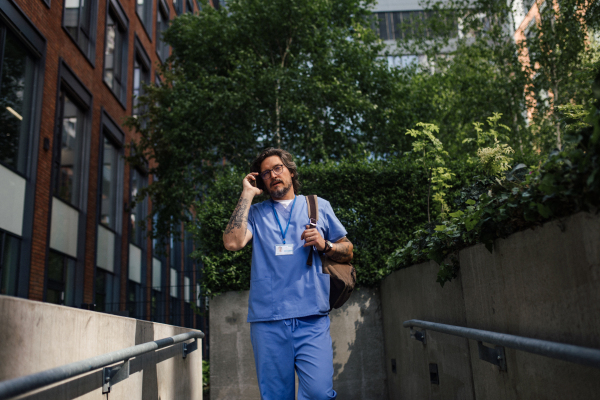 Male doctor in uniform going home from work, phone calling on smartphone. Work-life balance of healthcare worker.