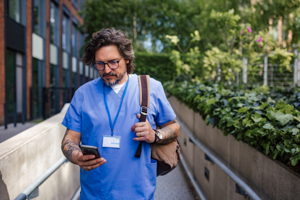 Male doctor in uniform going home from work, texting on smartphone. Work-life balance of healthcare worker.