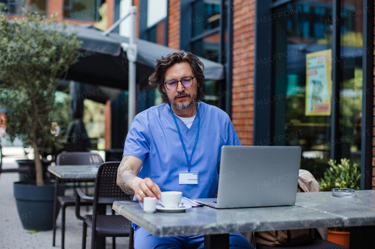 Doctor drinking coffee in coffee shop, working on laptop. Mental health and life balance for a healthcare worker. Telemedicine consultation online.