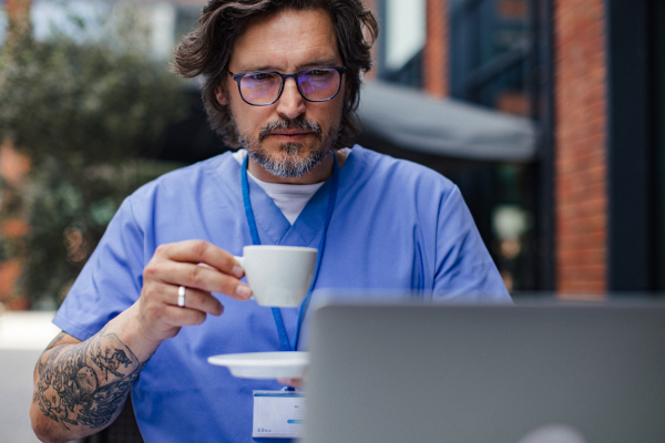 Doctor drinking coffee in coffee shop, working on laptop. Mental health and life balance for a healthcare worker. Telemedicine consultation online.