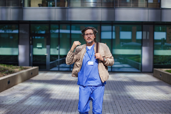 Male doctor in uniform going home from work, looking at camera. Work-life balance of healthcare worker.