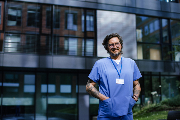 Portrait of handsome doctor in blue uniform outdoors. Work-life balance of healthcare worker.