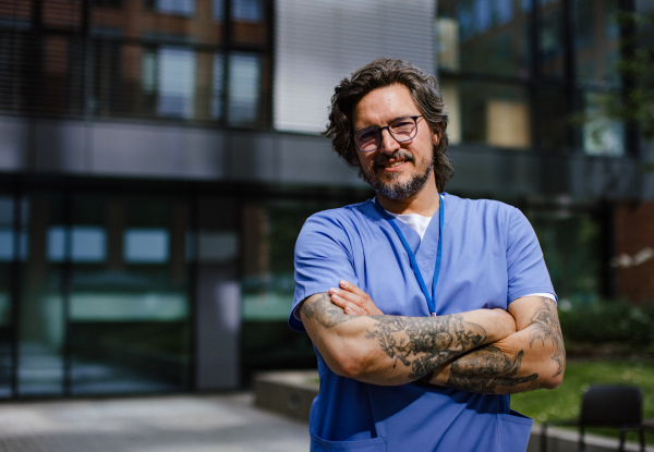 Portrait of handsome doctor in blue uniform outdoors. Work-life balance of healthcare worker.