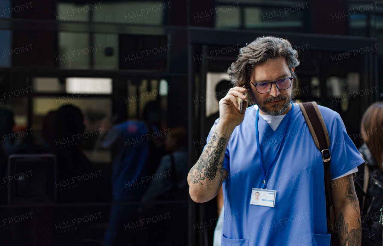 Male doctor in uniform going home from work, phone calling on smartphone. Work-life balance of healthcare worker.