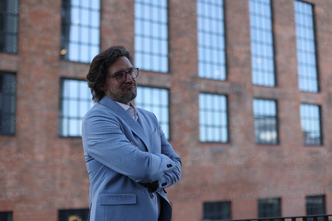 Portrait of mature businessman standing on city street, in front of office building. Handsome man with glasses in a suit.