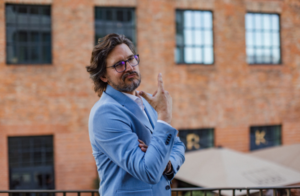 Portrait of mature businessman standing on city street, in front of office building. Handsome man with glasses in a suit.