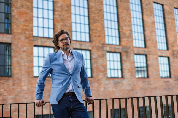 Portrait of mature businessman standing on city street, in front of office building. Handsome man with glasses in a suit.