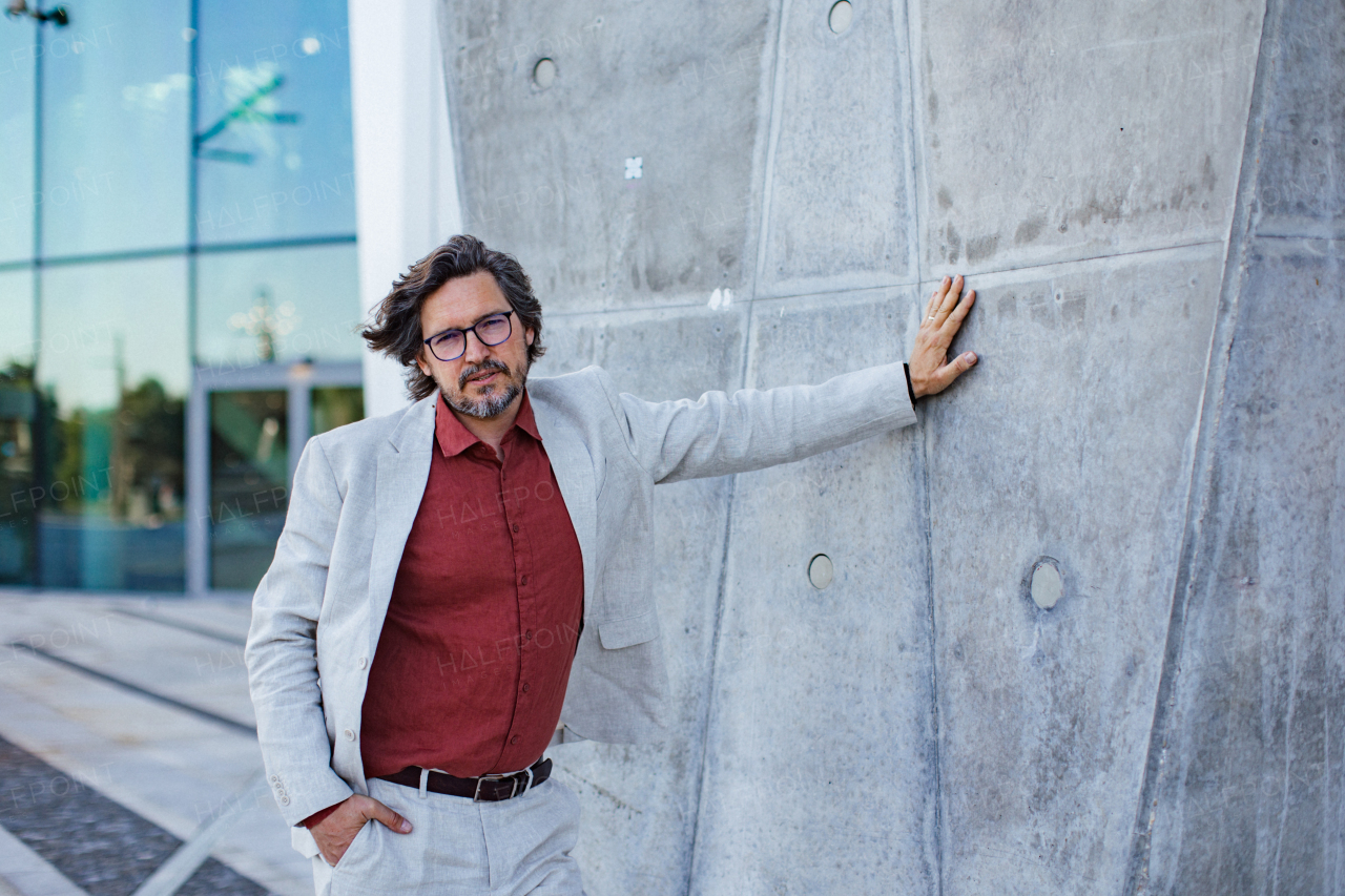 Portrait of mature businessman standing on city street, in front of office building. Handsome man with glasses in a suit.