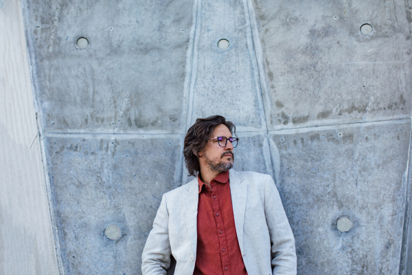 Portrait of mature businessman standing on city street, in front of office building. Handsome man with glasses in a suit.