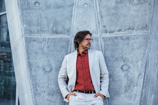 Portrait of mature businessman standing on city street, in front of office building. Handsome man with glasses in a suit.