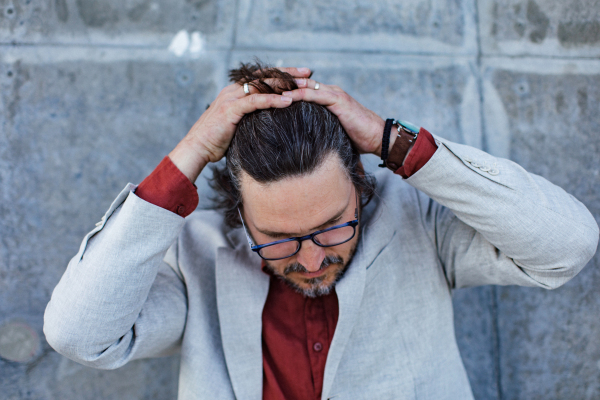 Portrait of mature businessman standing on city street, in front of office building. Handsome man with glasses in a suit.