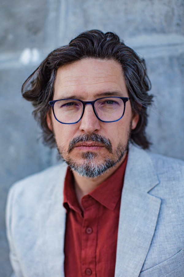 Portrait of mature businessman standing on city street, in front of office building. Handsome man with glasses in a suit.