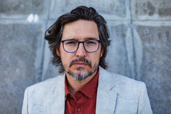 Portrait of mature businessman standing on city street, in front of office building. Handsome man with glasses in a suit.