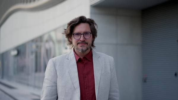 Video of mature businessman standing on city street, in front of office building. Handsome man with glasses in a suit.