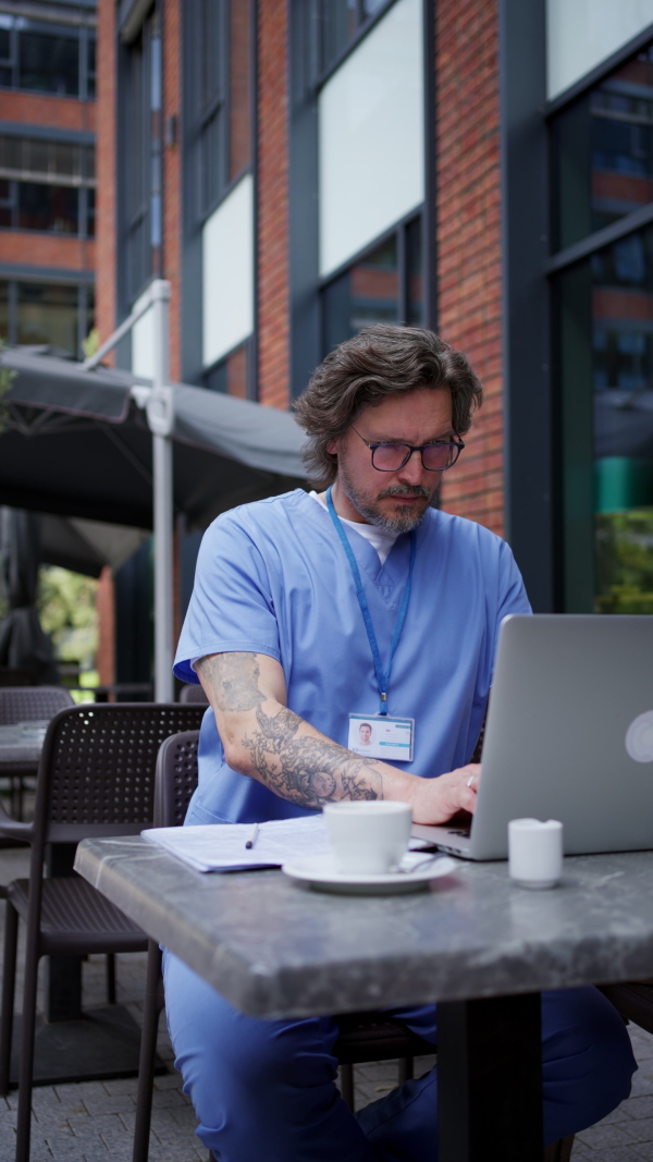 Doctor drinking coffee in coffee shop, working on laptop. Mental health and life balance for a healthcare worker. Telemedicine consultation online.