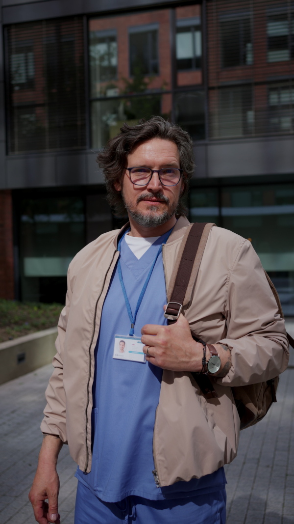 Male doctor in uniform going home from work, standing on parking lot, looking at camera. Work-life balance of healthcare worker.